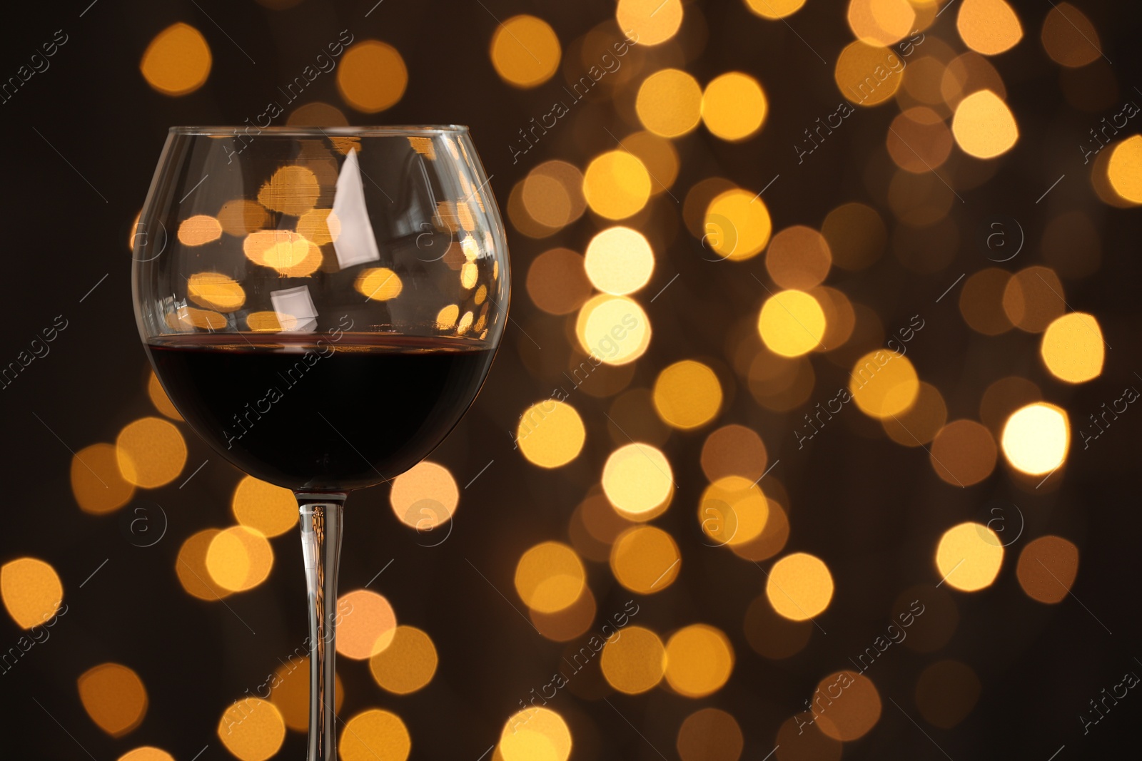 Photo of Tasty red wine in glass against dark background with blurred lights, closeup. Bokeh effect