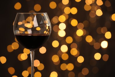 Photo of Tasty red wine in glass against dark background with blurred lights, closeup. Bokeh effect