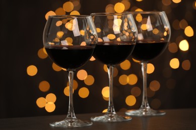 Photo of Tasty red wine in glasses on table against dark background with blurred lights, bokeh effect