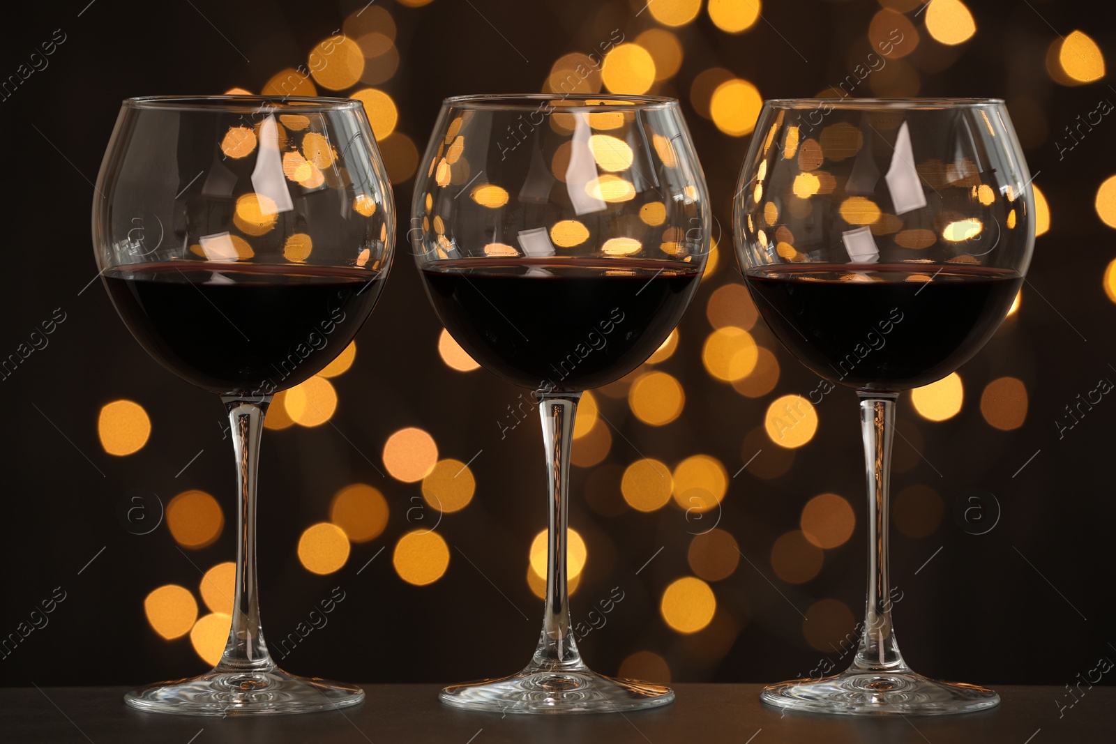 Photo of Tasty red wine in glasses on table against dark background with blurred lights, bokeh effect