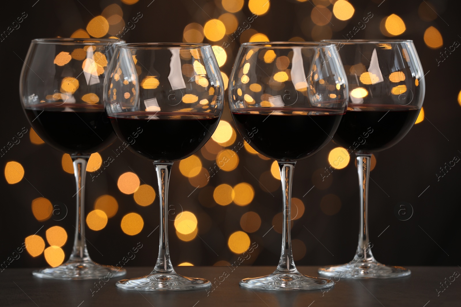 Photo of Tasty red wine in glasses on table against dark background with blurred lights, bokeh effect