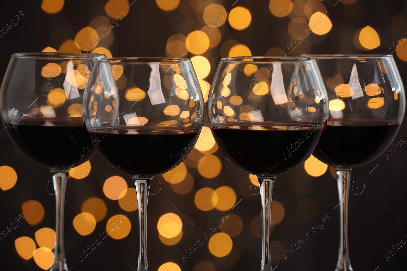 Photo of Tasty red wine in glasses against dark background with blurred lights, closeup. Bokeh effect