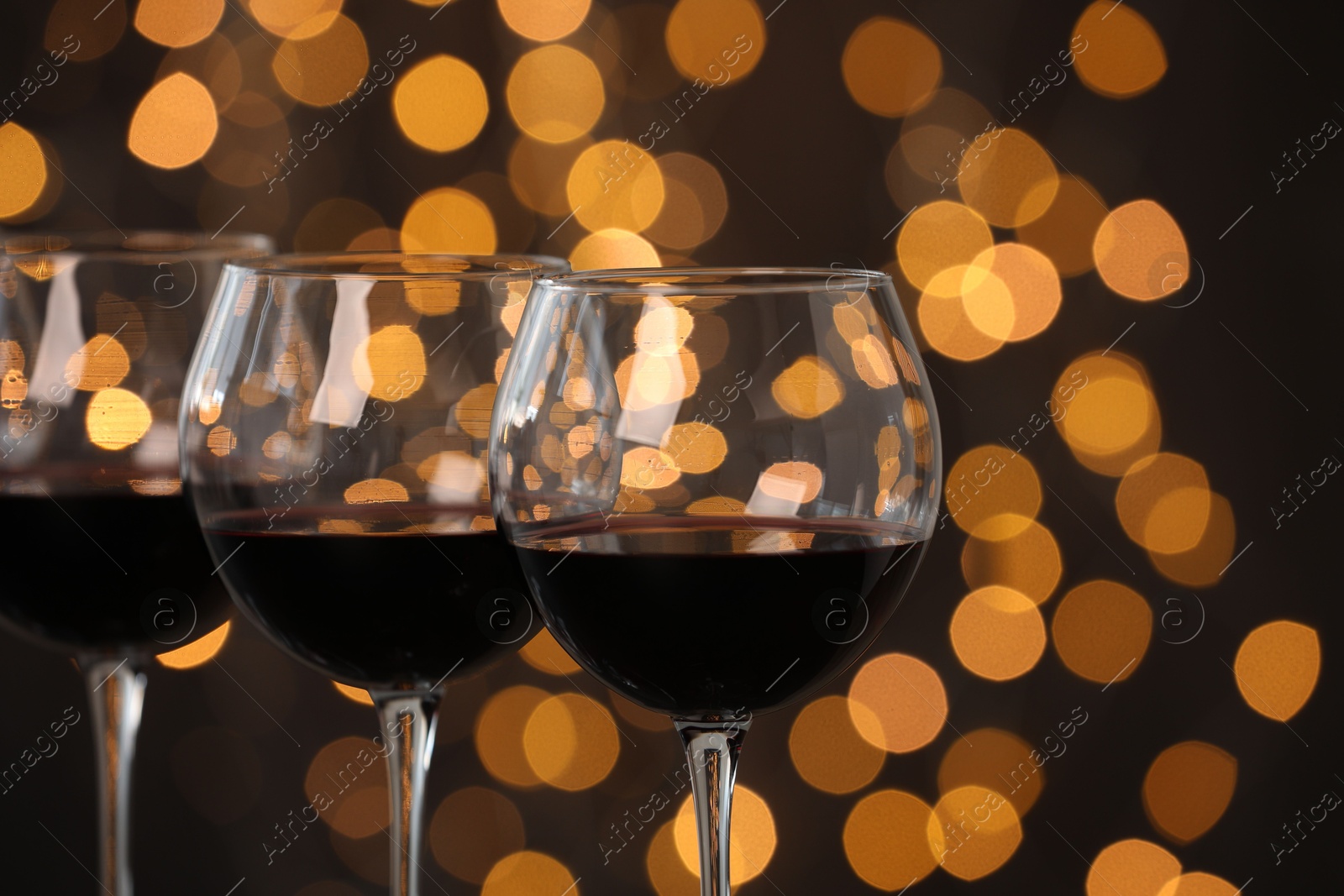 Photo of Tasty red wine in glasses against dark background with blurred lights, closeup. Bokeh effect