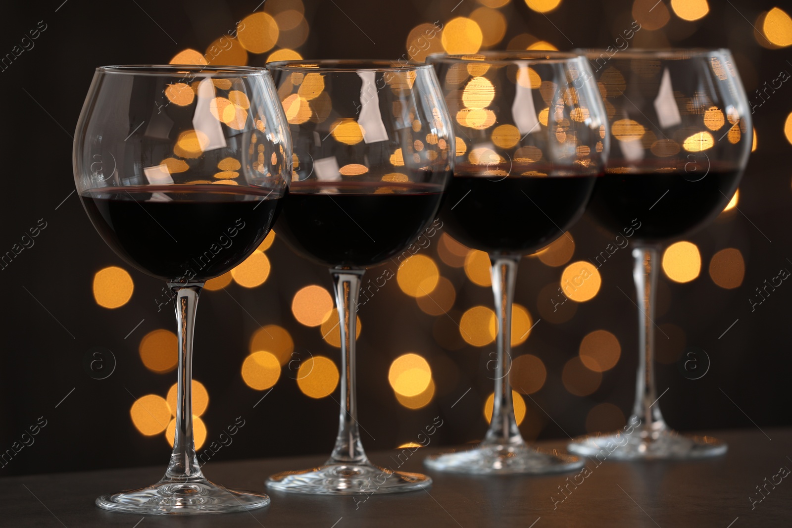 Photo of Tasty red wine in glasses on table against dark background with blurred lights, bokeh effect