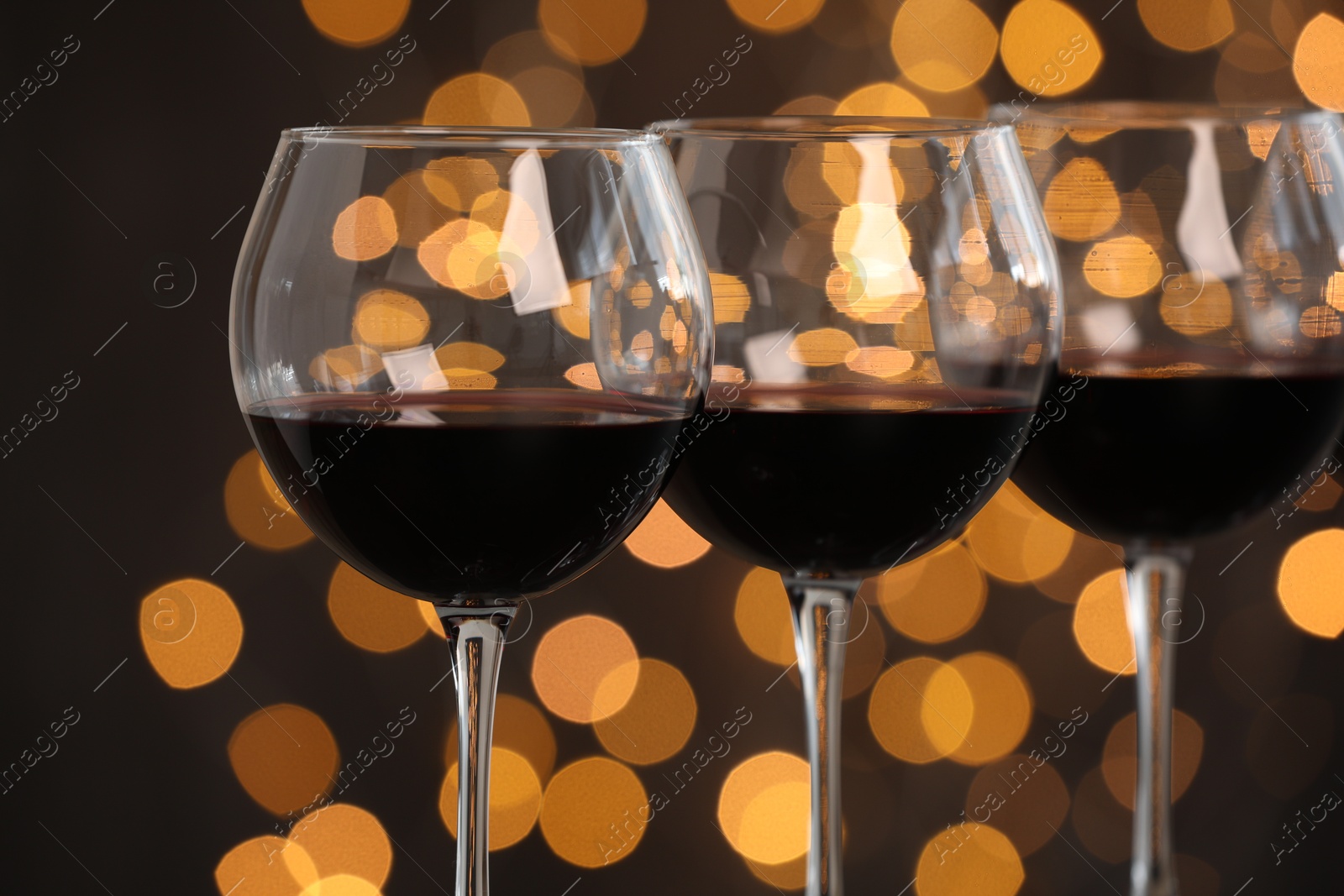 Photo of Tasty red wine in glasses against dark background with blurred lights, closeup. Bokeh effect