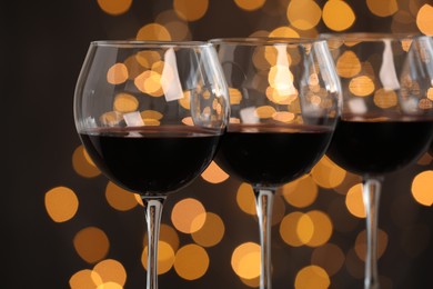 Photo of Tasty red wine in glasses against dark background with blurred lights, closeup. Bokeh effect