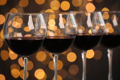 Photo of Tasty red wine in glasses against dark background with blurred lights, closeup. Bokeh effect