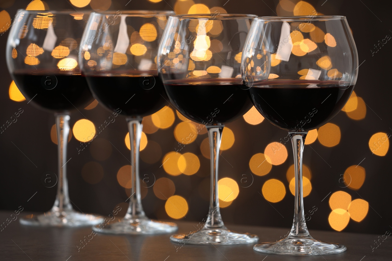 Photo of Tasty red wine in glasses on table against dark background with blurred lights, bokeh effect