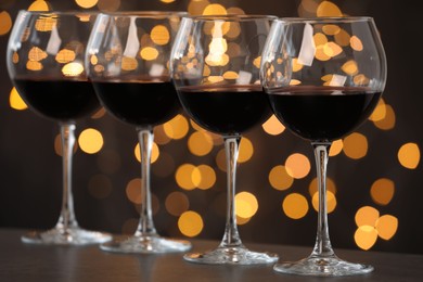 Photo of Tasty red wine in glasses on table against dark background with blurred lights, bokeh effect