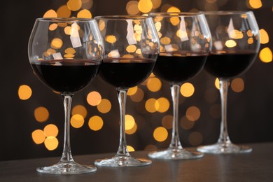 Photo of Tasty red wine in glasses on table against dark background with blurred lights, bokeh effect