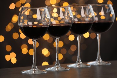 Photo of Tasty red wine in glasses on table against dark background with blurred lights, bokeh effect