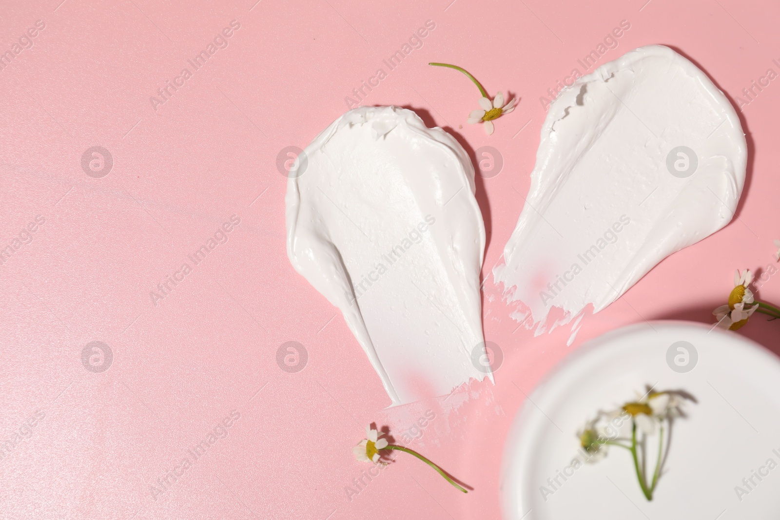 Photo of Samples of cream, jar and flowers on pink background, flat lay. Space for text