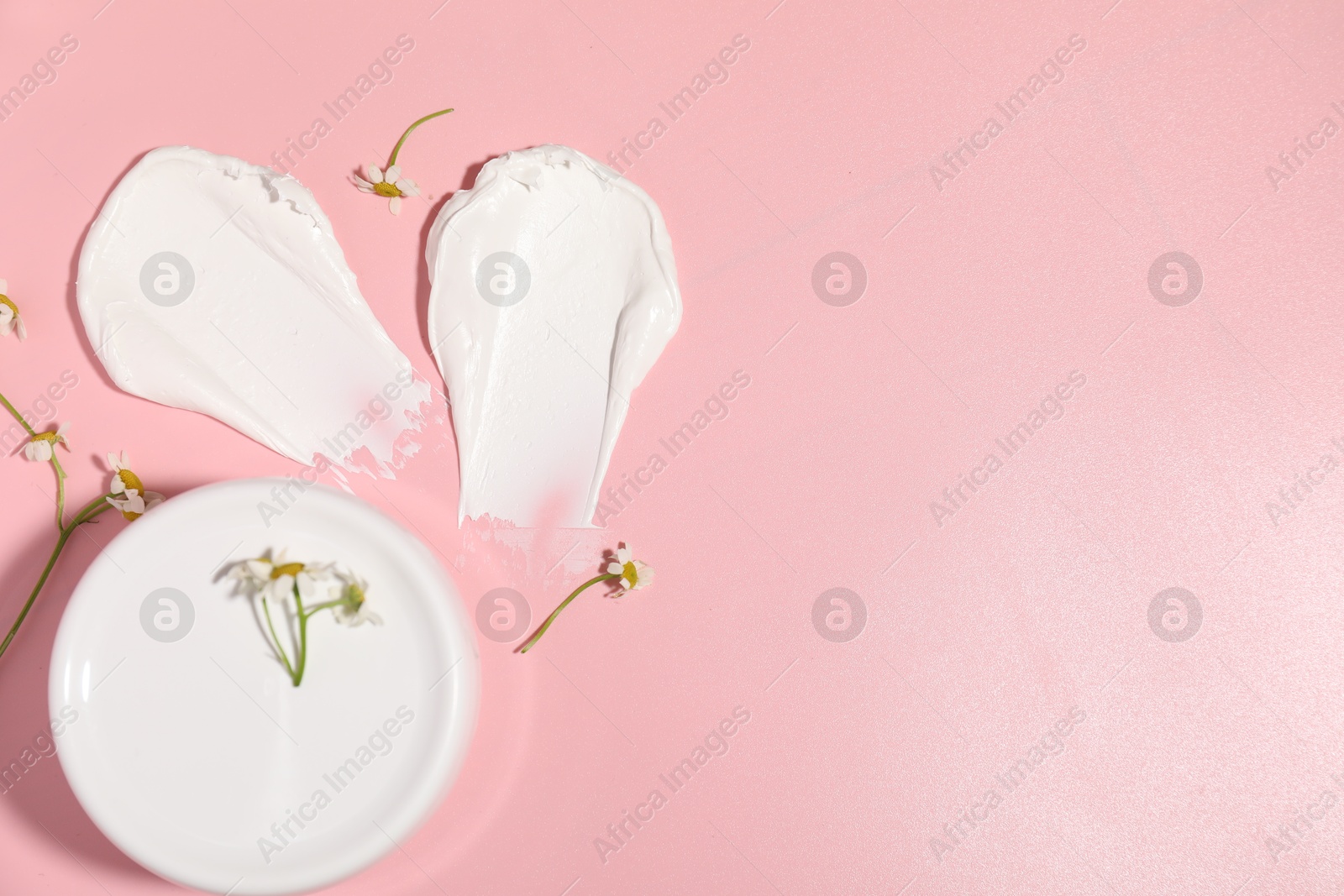 Photo of Samples of cream, jar and flowers on pink background, flat lay. Space for text