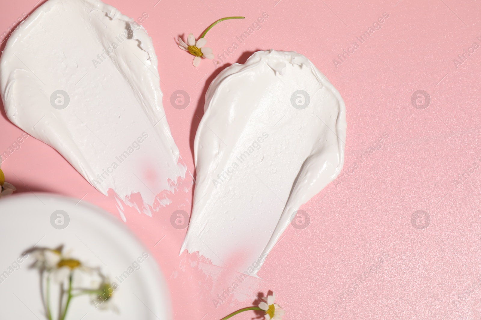 Photo of Samples of cream, jar and flowers on pink background, flat lay. Space for text