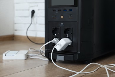 Photo of Modern portable power station with attached device indoors, closeup