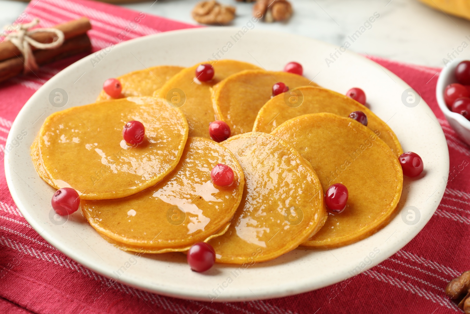 Photo of Tasty pumpkin pancakes with honey and cranberries on table, closeup