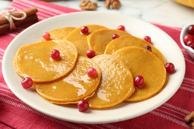 Photo of Tasty pumpkin pancakes with honey and cranberries on table, closeup