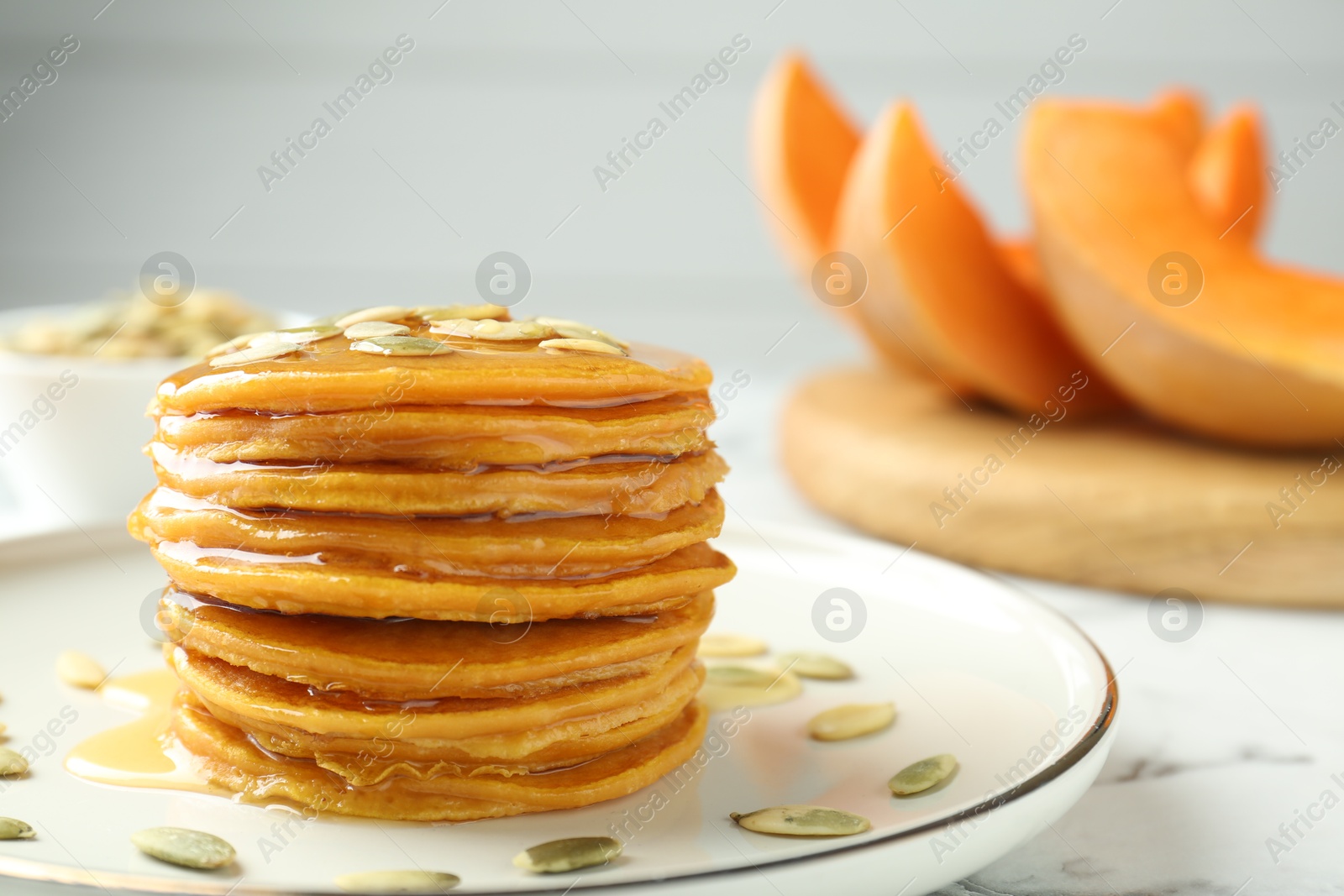 Photo of Tasty pumpkin pancakes with seeds on white marble table, closeup