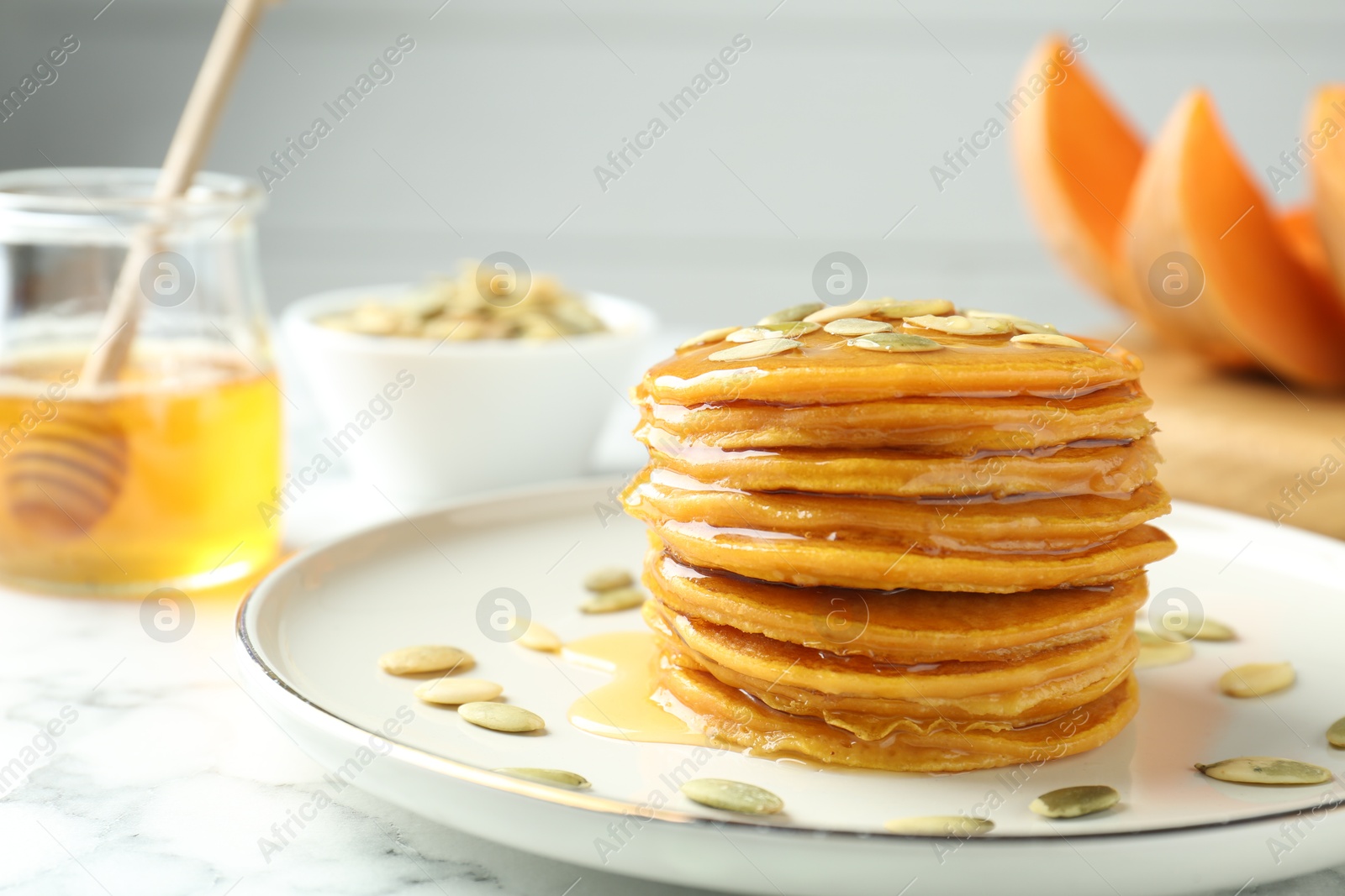 Photo of Tasty pumpkin pancakes with seeds on white marble table, closeup