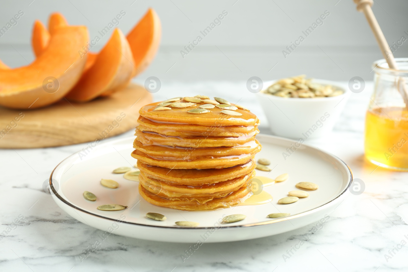 Photo of Tasty pumpkin pancakes with seeds on white marble table, closeup