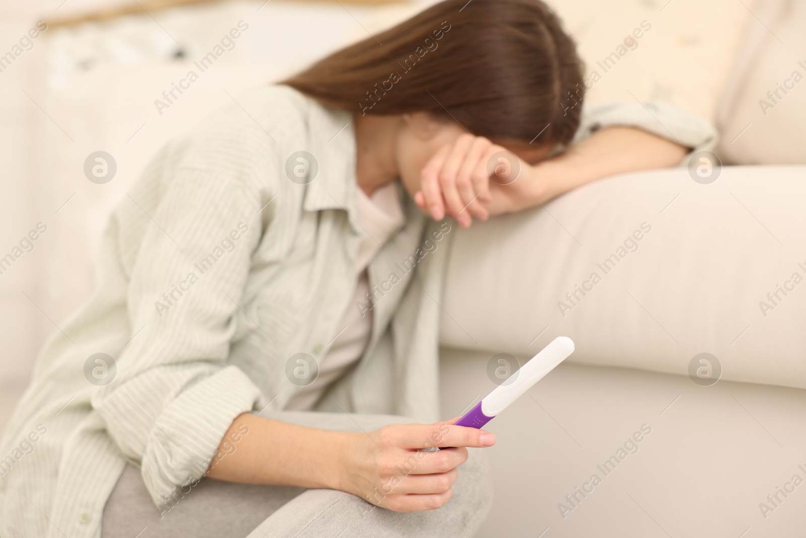 Photo of Upset woman with negative pregnancy test at home, selective focus