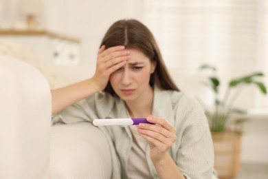 Photo of Upset woman with negative pregnancy test at home, selective focus