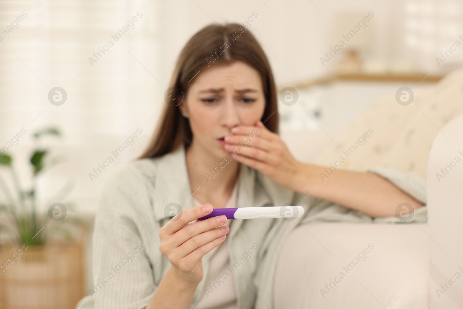 Photo of Upset woman with negative pregnancy test at home, selective focus