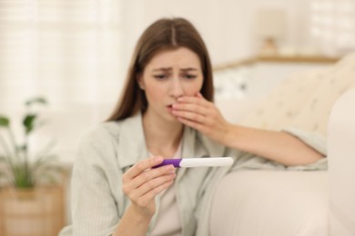 Photo of Upset woman with negative pregnancy test at home, selective focus