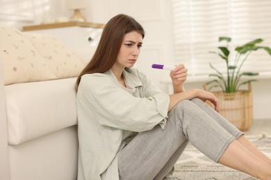 Photo of Upset woman with negative pregnancy test at home