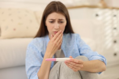 Photo of Upset woman with negative pregnancy test at home, selective focus