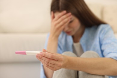 Photo of Upset woman with negative pregnancy test at home, selective focus