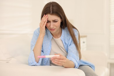 Photo of Upset woman with negative pregnancy test on sofa at home