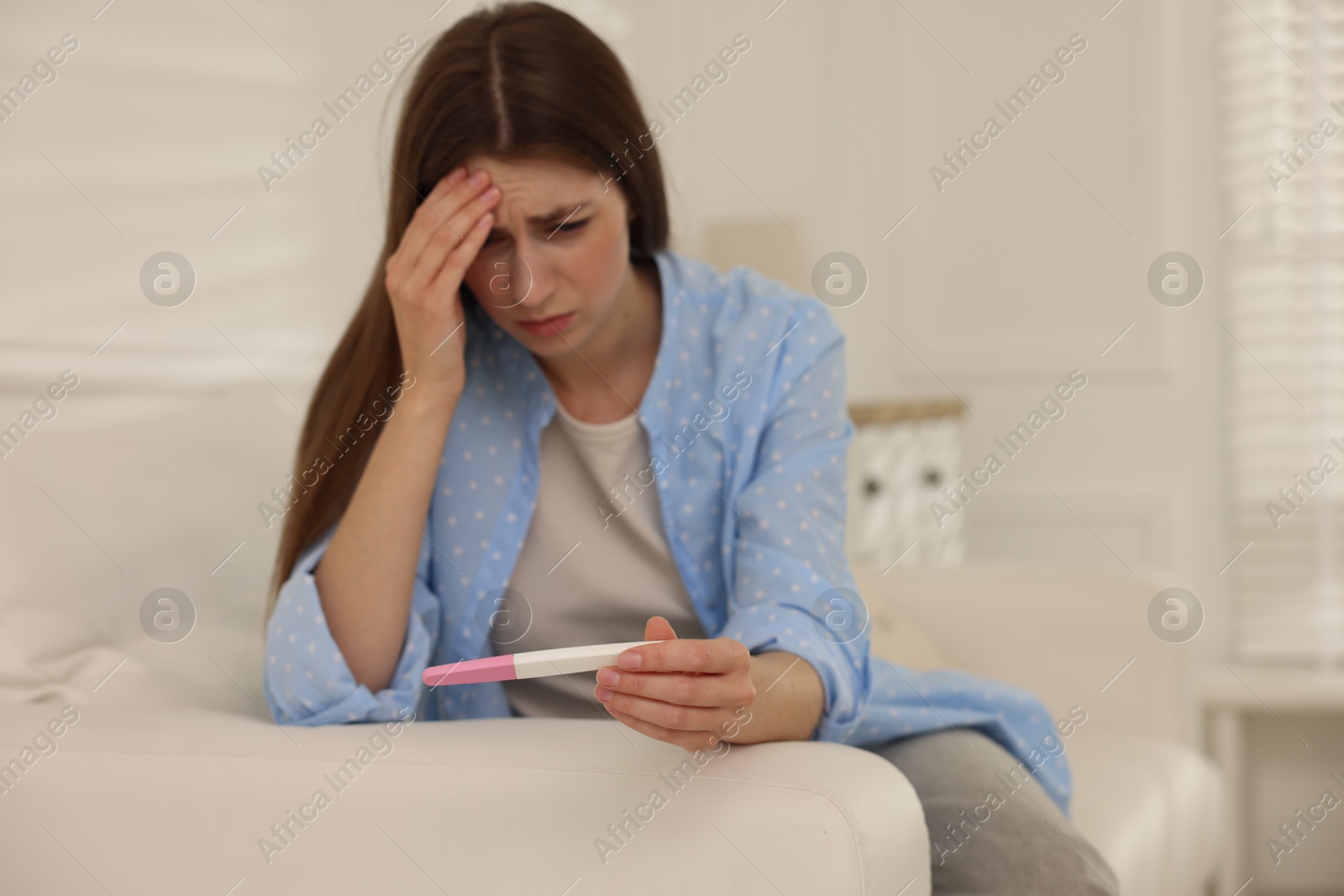 Photo of Upset woman with negative pregnancy test on sofa at home, space for text