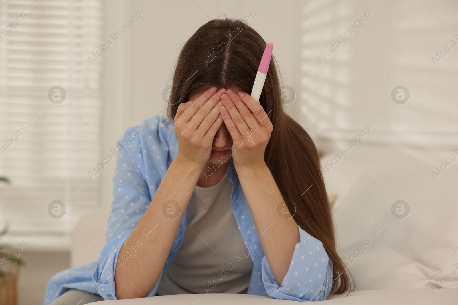 Photo of Upset woman with negative pregnancy test on sofa at home