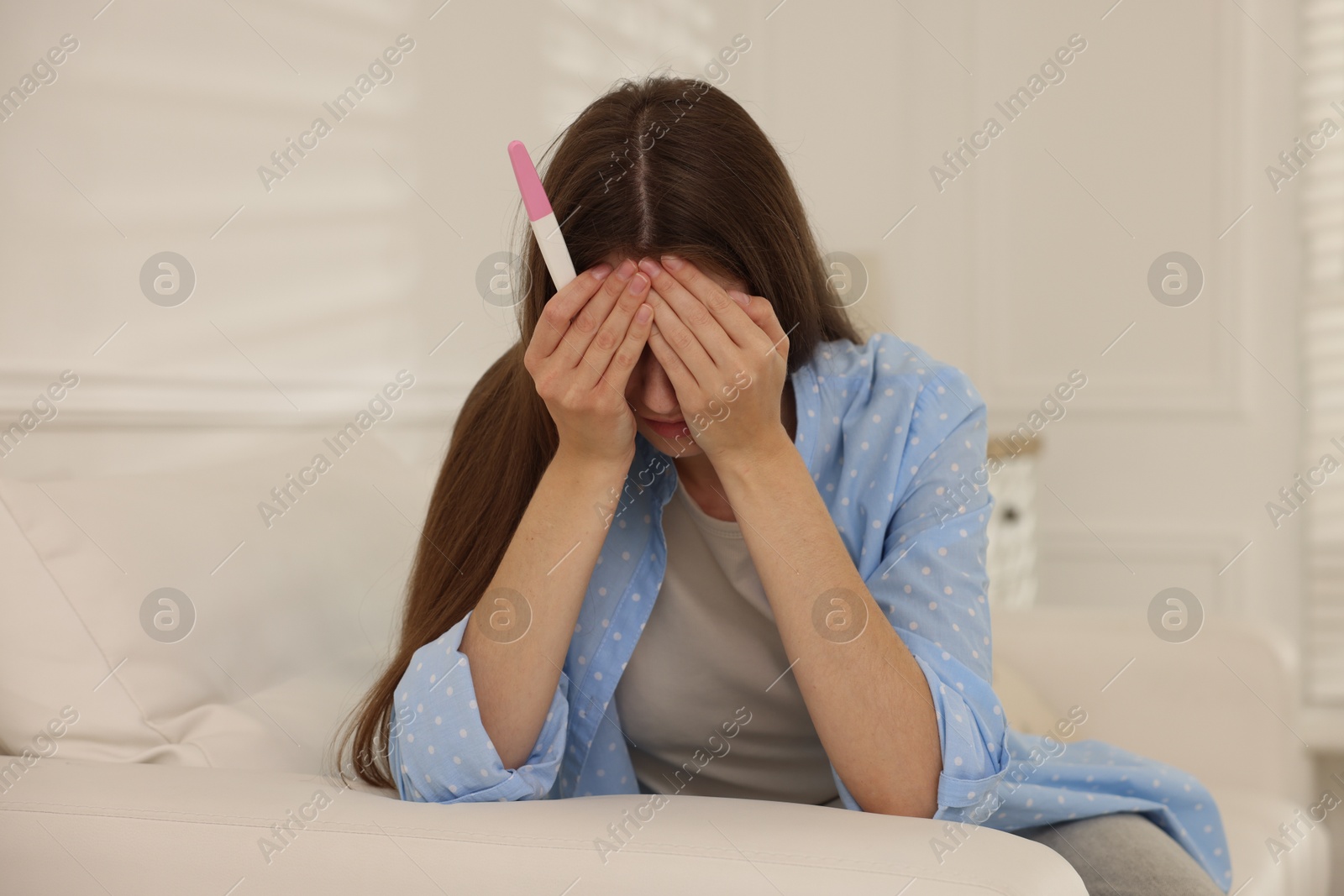 Photo of Upset woman with negative pregnancy test on sofa at home