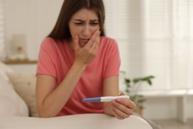 Photo of Upset woman with negative pregnancy test on sofa at home, selective focus. Space for text