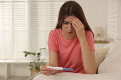 Photo of Upset woman with negative pregnancy test on sofa at home, space for text