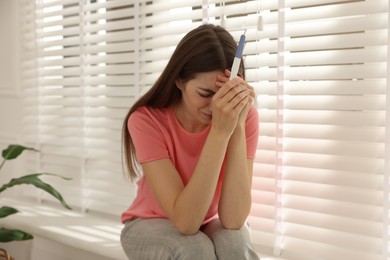 Photo of Upset woman with negative pregnancy test near window at home, selective focus