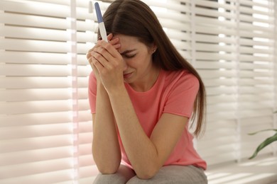 Photo of Upset woman with negative pregnancy test near window at home, selective focus