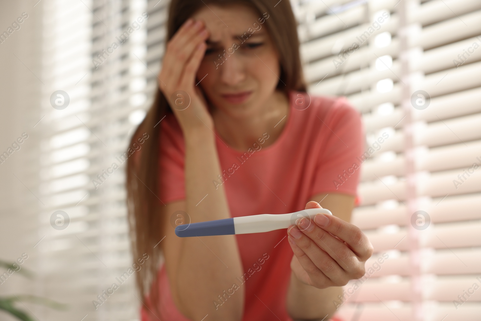 Photo of Upset woman with negative pregnancy test near window at home, selective focus