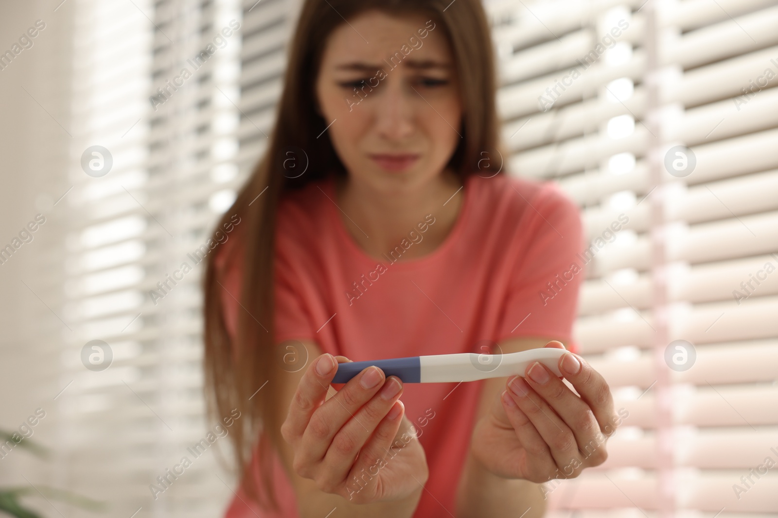 Photo of Upset woman with negative pregnancy test near window at home, selective focus