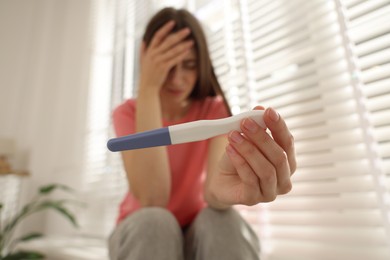 Photo of Upset woman with negative pregnancy test near window at home, selective focus