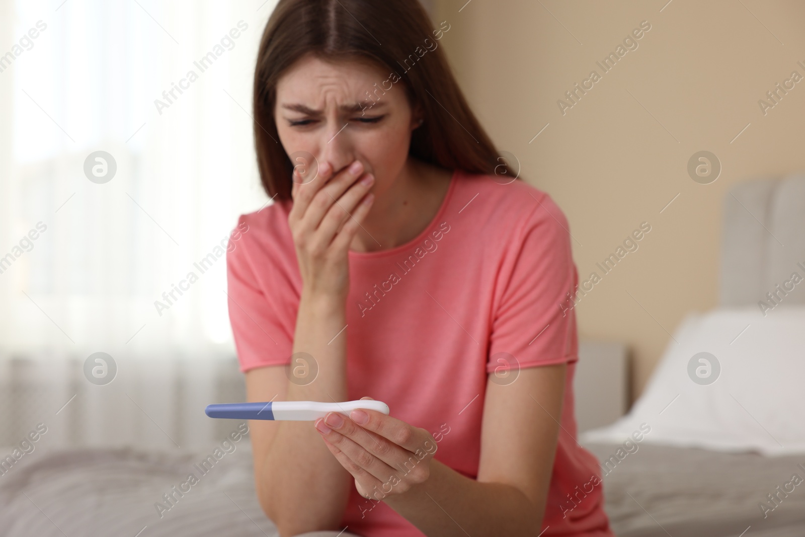 Photo of Upset woman with negative pregnancy test on bed at home