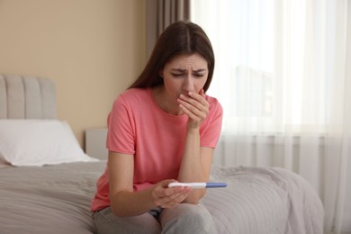 Photo of Upset woman with negative pregnancy test on bed at home