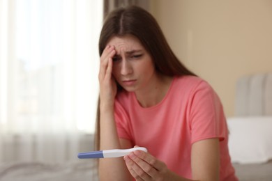 Photo of Upset woman with negative pregnancy test at home, selective focus. Space for text