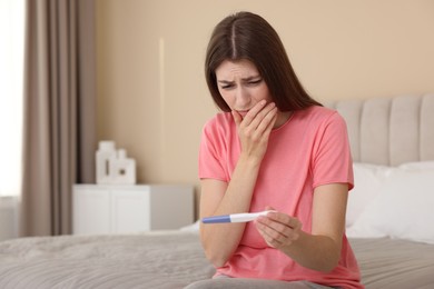 Photo of Upset woman with negative pregnancy test on bed at home, space for text