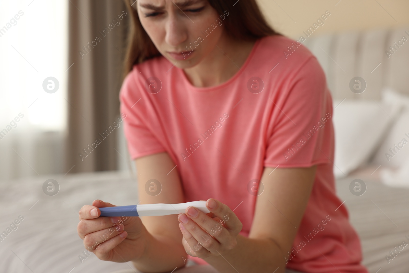 Photo of Upset woman with negative pregnancy test on bed at home