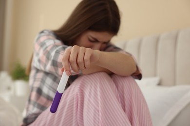 Photo of Upset woman with negative pregnancy test on bed at home, selective focus