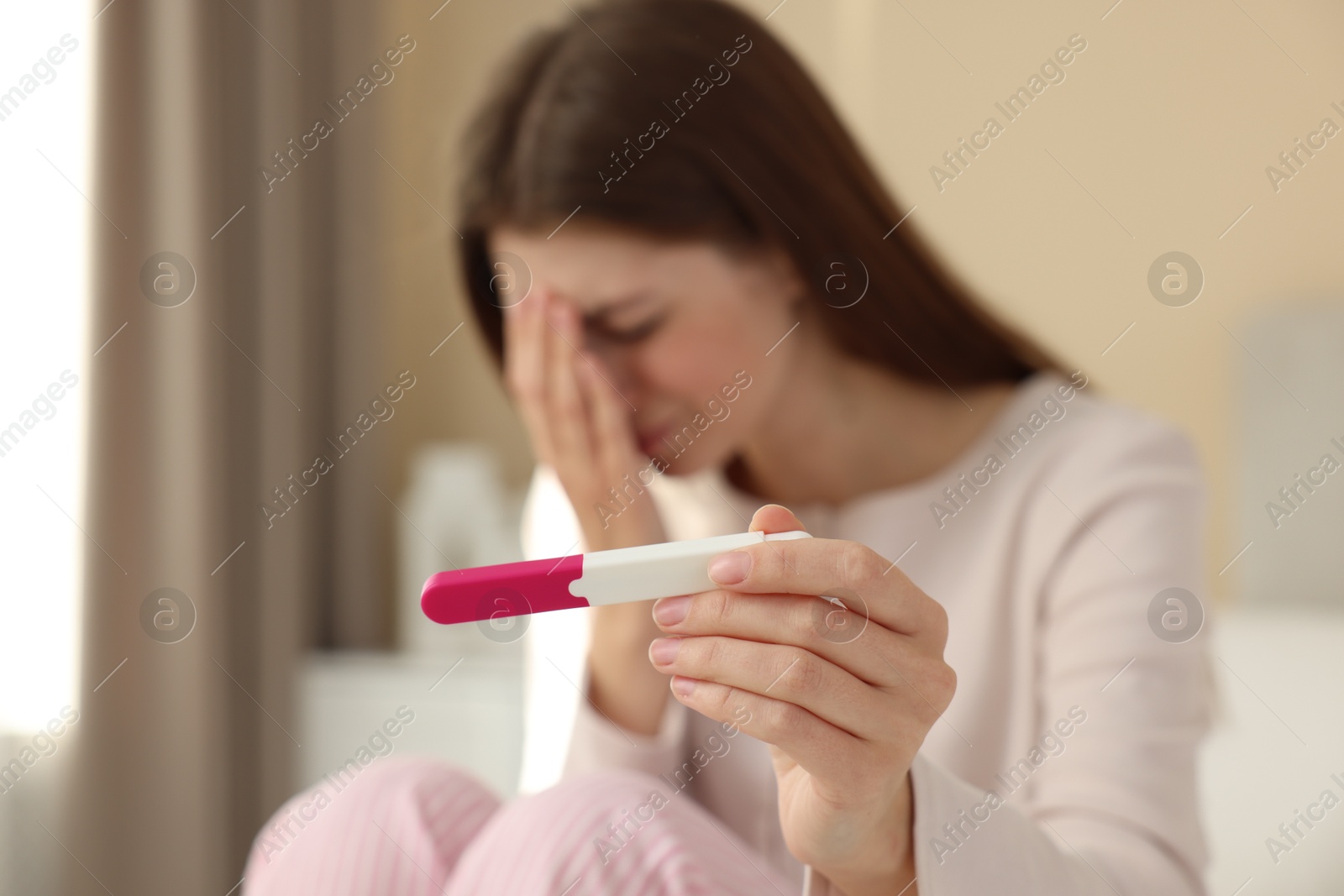 Photo of Upset woman with negative pregnancy test at home, selective focus