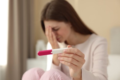 Photo of Upset woman with negative pregnancy test at home, selective focus